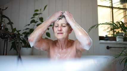 Contented senior woman washing in bubble bath tub at home, eyes closed.