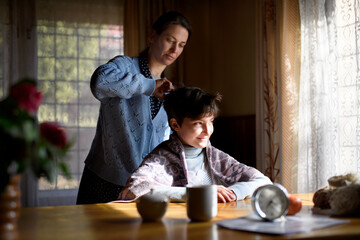 Portrait of poor woman cutting daughter's hair indoors at home, poverty concept.