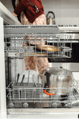 The housewife puts the dishes in the dishwasher. Kitchen interier.