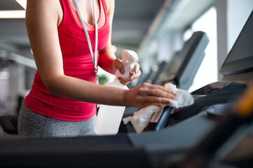 Midsection of fitness instructor disinfecting equipment in gym, coronavirus concept.