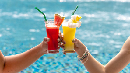 Hands of young couple toasting fruit juice drinks or cocktails to spend happy time or celebrate together by  swimming pool at a resort
