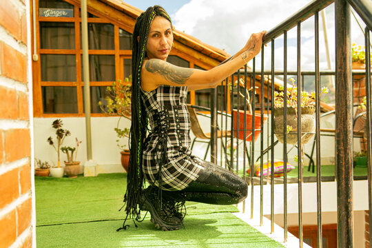 Mujer transg&eacute;nero con trenzas agachada y sujetada de la baranda de la escalera en su terraza 