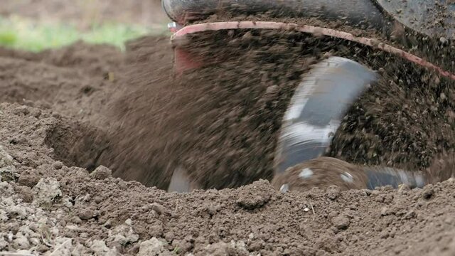Tiller engine working in garden in SLOW MOTION HD VIDEO.&nbsp;Cultivator machine cultivating field at spring.&nbsp;Extreme close-up of soil throwing away of blades. Modern farming, technology agriculture.