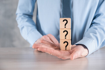 Businessman hold and put wooden cube block shape with question marks on grey table. Space for...