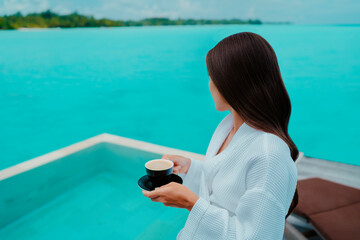 Woman having breakfast at luxury hotel room drinking coffee cup with view of turquoise ocean and...