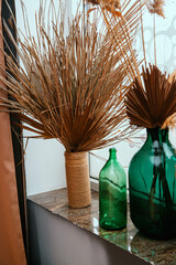 Dried palm leaves and reed branches in glass jars. Home decor stands on the windowsill.