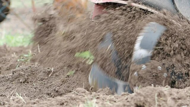Tiller engine working in garden in SLOW MOTION HD VIDEO.&nbsp;Cultivator machine cultivating field at spring.&nbsp;Extreme close-up of soil throwing away of blades. Modern farming, technology agriculture.
