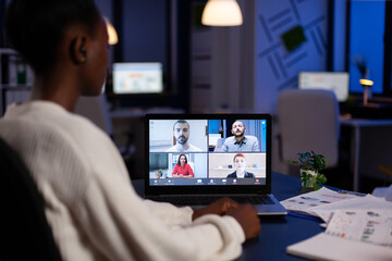 African businesswoman talking during video conference with team in midnight using laptop in start up business office. Diverse workers talking during corporate meeting using technology network wireless