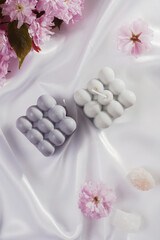 A grey-blue bubble candle on a white silky fabric and pink cherry blossom in the background, top view