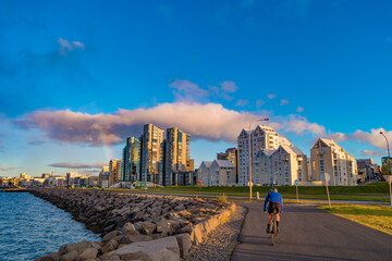 Cityscape over Reykjavik business and touristic downtown, embankment, ocean, harbor, modern buildings with cyclist at cycling lane at sunset skyline, Iceland, summer. - obrazy, fototapety, plakaty