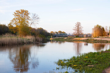 Fototapeta premium Natural landscape by the river, on a sunny spring evening, with a river, trees and grass. Spring peace and harmony has flourished.