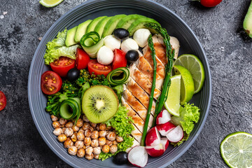 Grilled chicken, avocado, asparagus, chickpeas, broccoli, radish, chicken, cucumber, tomatoes, olives, mozzarella buddha bowl on dark background, top view. Delicious balanced food concept