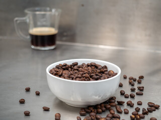 Roasted coffee beans in white bowl with americano in glass cup on table