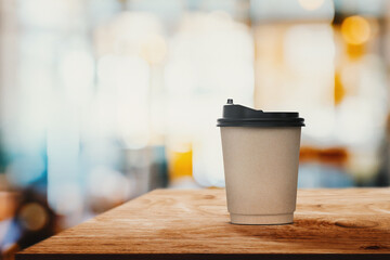 Paper coffee cup on wood table with abstract blur interior coffee shop or cafe for background.