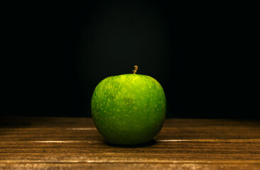 green apple on a wooden board on a black background. front view