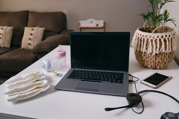 workplace of a working mother at home with baby items on her white table with laptop, mobile phone and headphones on the table