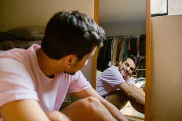Hombre joven gay sonriendo a si mismo frente al espejo 