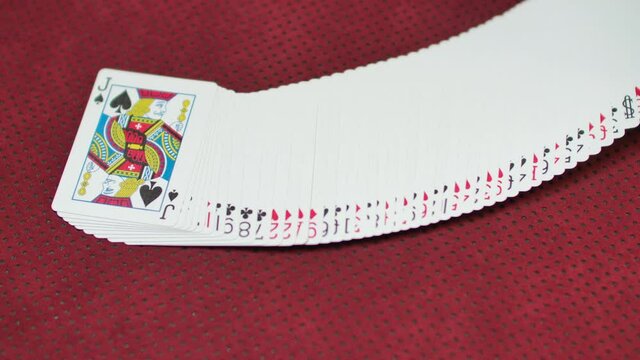 Slow motion closeup of a a deck of cards being spread on a red game table.