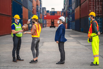 Professional of group cargo foreman in helmets standing and using infrared thermometer for checking body temperature staff fever before work in quarantine for coronavirus wearing protective mask
