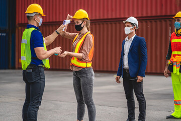 Professional of group cargo foreman in helmets standing and using infrared thermometer for checking body temperature staff fever before work in quarantine for coronavirus wearing protective mask