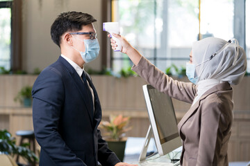 An employee at the company, wearing a mask to prevent the virus, is taking an infrared thermometer to measure the temperature.