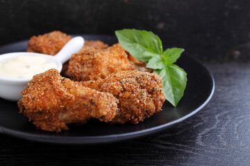 Crispy fried chicken wings with sauce on black background.
