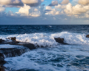 White water running over rocks in the blue ocean on a fall evening in Qawra, Malta.