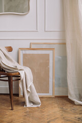 Stylish interior of living room with wooden empty poster frames on parquet, chair and linen blanket. Modern home decor. Template, mock up.