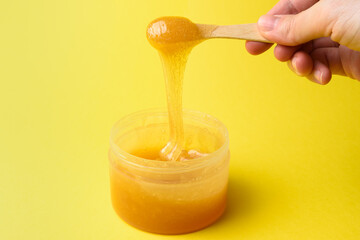 Liquid sugar wax in plastic jar with wooden spatula in hand close up on yellow