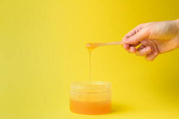 Liquid sugar wax in plastic jar with wooden spatula in hand on yellow