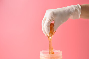 Hand in glove with sugar wax piece from jar on pink