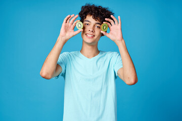 Cheerful guy with curly hair kiwi fruit blue background