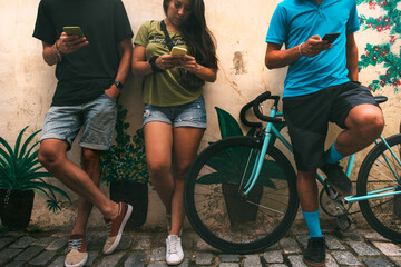 group of friends on the street with a bicycle busy each with his mobile phone stacked on a wall...