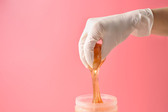 Hand in glove with sugar wax piece from jar on pink