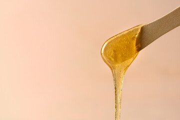 Liquid yellow sugar paste or wax for epilation on wooden stick or spatula closeup - obrazy, fototapety, plakaty