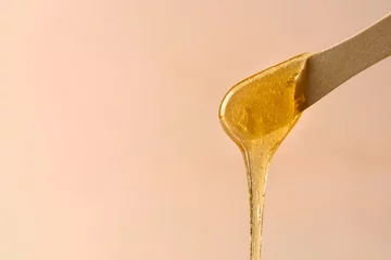 Fotobehang Liquid yellow sugar paste or wax for epilation on wooden stick or spatula closeup © molenira