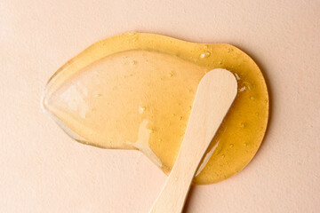 Liquid sugar wax smear with spatula on beige background - obrazy, fototapety, plakaty