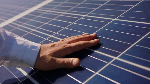 Close up of a young engineer hand is checking the operation of sun and cleanliness of photovoltaic solar panels on a sunset. Concept.renewable energy, technology, electricity, service, green, future