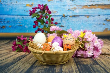 Color eggs decorated with wax and glitter in a basket and branches of ornamental cherries.