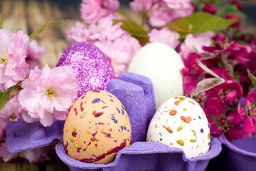 Four eggs decorated with wax and glitter in a purple egg wrapper and branches of ornamental cherries.