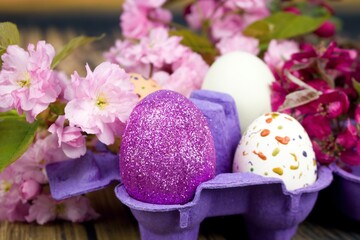 Obraz na płótnie Canvas Four eggs decorated with wax and glitter in a purple egg wrapper and branches of ornamental cherries.