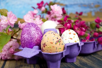 Four eggs decorated with wax and glitter in a purple egg wrapper and branches of ornamental...