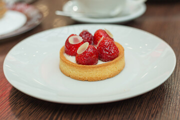 Freshly baked tartlet with fresh strawberry, cream, almond on white plate. Summer dessert. Close up with shallow dof.