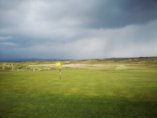 Golf course in the rain with a yellow flag on the green - Porthcawl. 