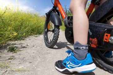 Boy cycling on a dirt road surrounded by flowers. Detail of a children's bike wheel