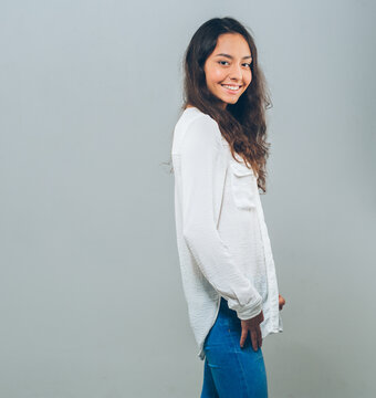 Beautiful brunette woman with long hair in white shirt and jeanse over gray background happy smile teeth