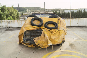 Old abandoned pickup truck covered with a yellow tarpaulin at a car park
