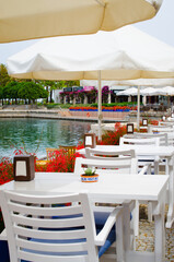White tables and chairs on the terrace of a cozy summer cafe overlooking the water.