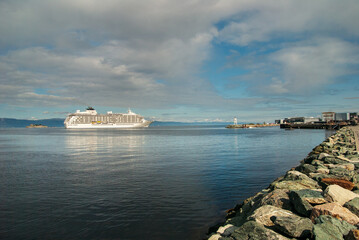 View of the seaside of Trondheim, Norway. A big white cruise ship in the background, reflected in calm sea. Blue sky with white clouds on a sunny day.