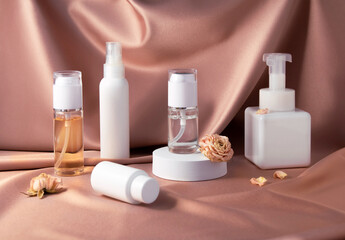 Cosmetic products and dry rose on pink shiny textile background. White and clear bottles of face and body products. Beauty concept